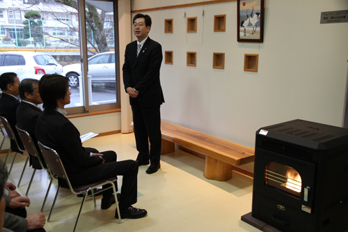 ストーブの横であいさつをする勝又支店長
