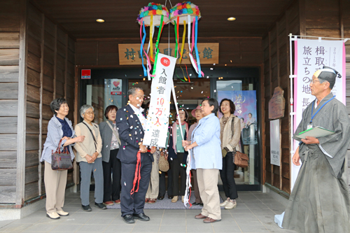 10万人目となった日置むつみ学級を代表して萩野谷ミサ子さんがくす玉を割る