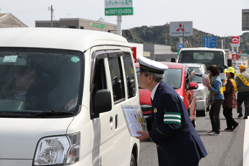 信号で立ち止まったドライバーに交通安全啓発グッズを手渡す