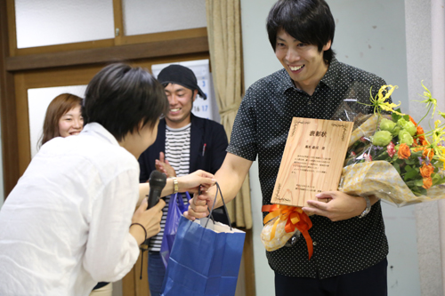 地域おこし協力隊のメンバーから、花束や木で作られた表彰状の贈呈を受ける馬來さん（右）