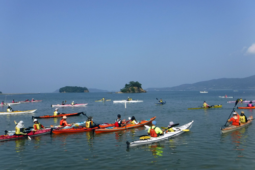 快晴のもと、一斉に油谷湾に漕ぎ出す参加者ら