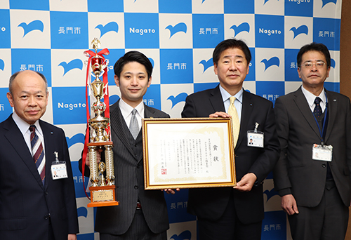 グランプリのトロフィーと賞状をもって来訪した油谷湾温泉ホテル楊貴館の岡藤さん
