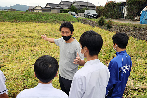 ほ場で深川中学校の生徒に説明する山本さん