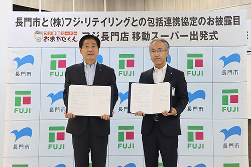 協定書を掲げる江原市長と株式会社フジ・リテイリングの向井雅彦執行役員（山口運営事業部長）