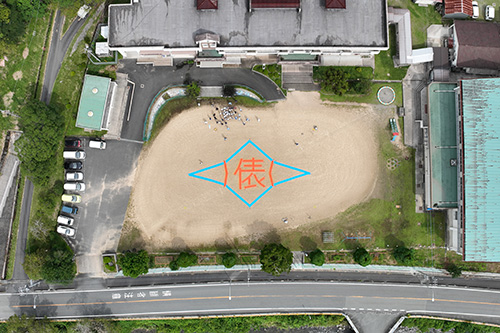 グラウンドに描かれた校章と児童ら（ドローンによる空撮写真）