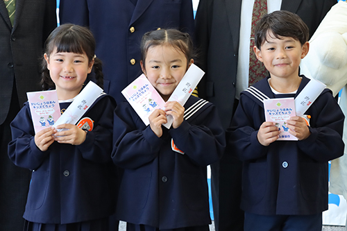 手帳と記念品の鉛筆を手に笑顔の新１年制