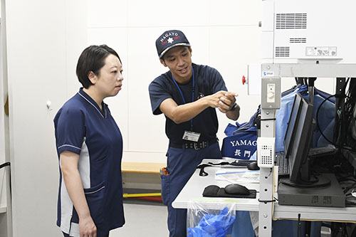 通報から出動までの流れについて説明を受ける永井看護師（左）